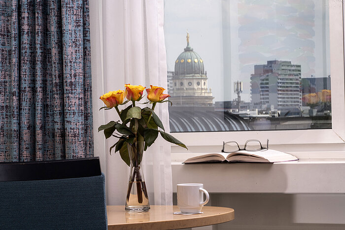 Room detail Vase with yellow roses, book and cup by window overlooking Französischer Dom at Maritim proArte Hotel Berlin
