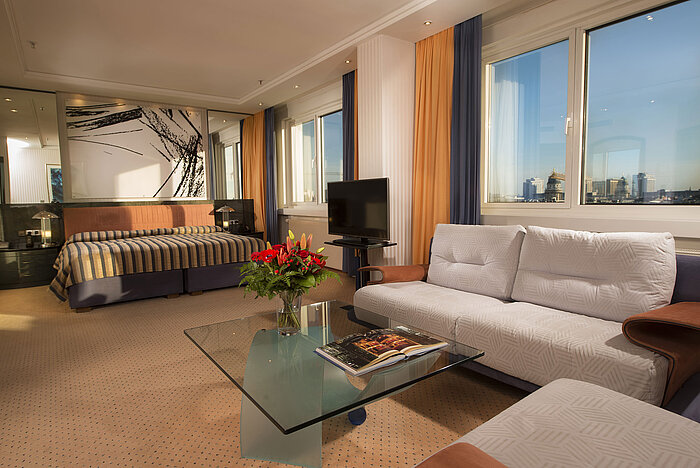 Peter Kuckei Suite Kuckei Suite at Maritim proArte Hotel Berlin with sofa, glass coffee table, and large window overlooking Berlin skyline.